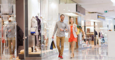 sale, consumerism and people concept - happy young couple with shopping bags walking in mall