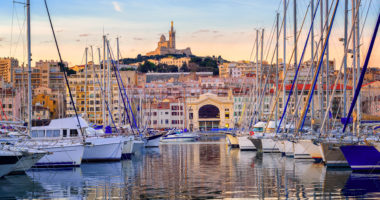 Yachts reflecting in the still water of the old Vieux Port of Marseilles beneath Cathedral of Notre Dame, France, on sunrise