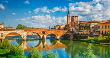 Panoramic view to Bridge Ponte Pietra in Verona on Adige river, Veneto region, Italy. Sunny summer day panorama and blue dramatic sky with clouds. Ancient european italian terracotta color houses.