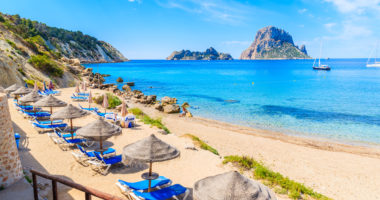View of Cala d'Hort beach with sunbeds and umbrellas and beautiful azure blue sea water, Ibiza island, Spain