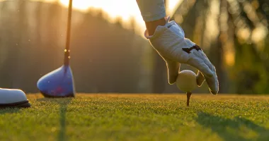 Hand asian woman putting golf ball on tee with club in golf course on evening and sunset time a for healthy sport.  Lifestyle Concept