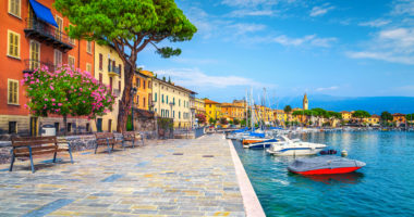 Wonderful paved walkway with colorful mediterranean flowers. Luxury yachts, boats and sailing boats in the majestic harbor of Toscolano-Maderno, lake Garda, Lombardy region, Italy, Europe