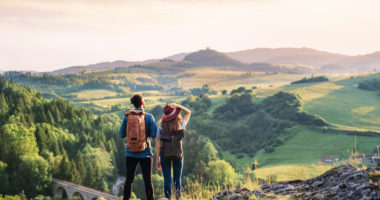 Rear view of young tourist couple travellers with backpacks hiking in nature, resting.