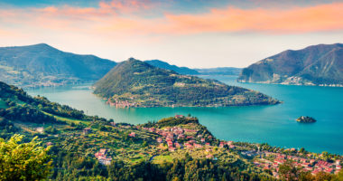 Panoramic summer view of Iseo lake. Impressive sunrise on Marone town with Monte Isola island, Province of Brescia, Italy, Europe. Traveling concept background.