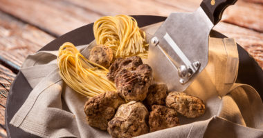 Alba white truffles in napkin with raw egg tagliolini and steel truffle cutter on wooden background
